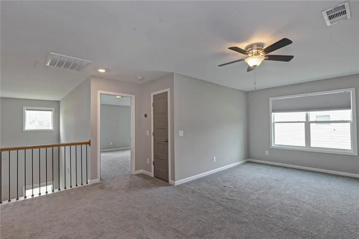A well-lit upper level space with soft gray carpeting and a practical ceiling fan for comfort.