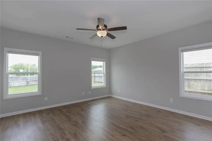 A well-lit bedroom features durable laminate flooring and a ceiling fan for comfort.