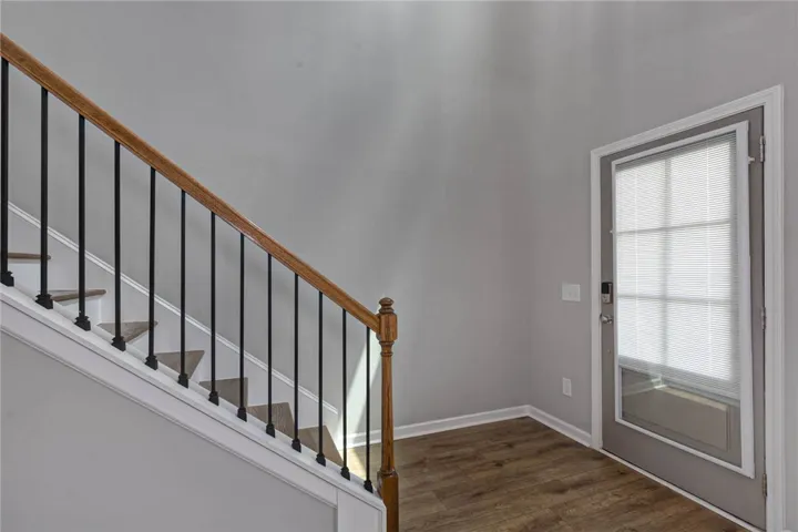 A graceful staircase with wood and iron accents leads to upper levels, beside a sun-lit entry with rich wood flooring.