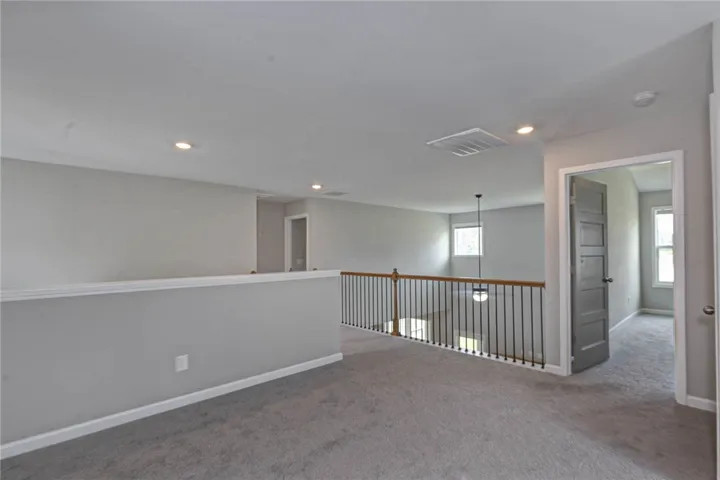 An airy loft area features neutral carpeting and bright recessed lighting.