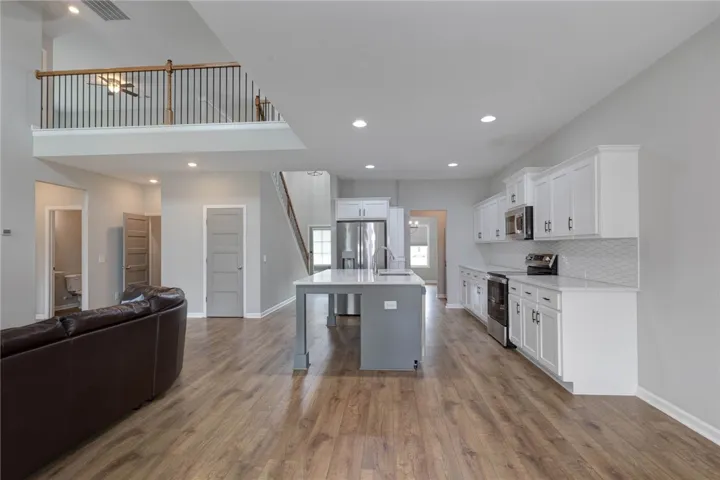An open-concept living area seamlessly connects the kitchen with a spacious common area, featuring a two-story ceiling and contemporary wood flooring.