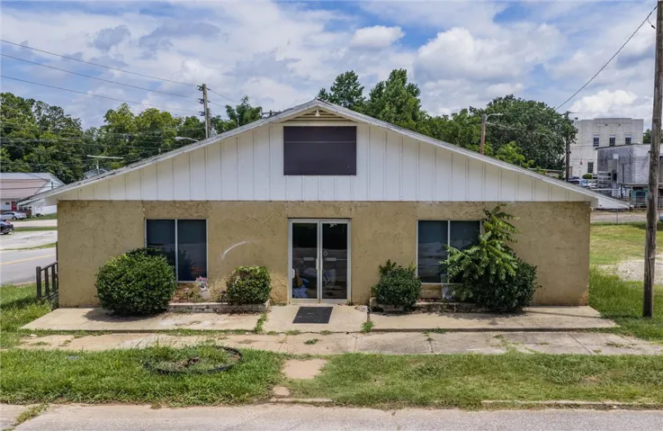 A modest commercial building featuring a stucco exterior and a distinctive gabled roofline, nestled amidst mature trees.
