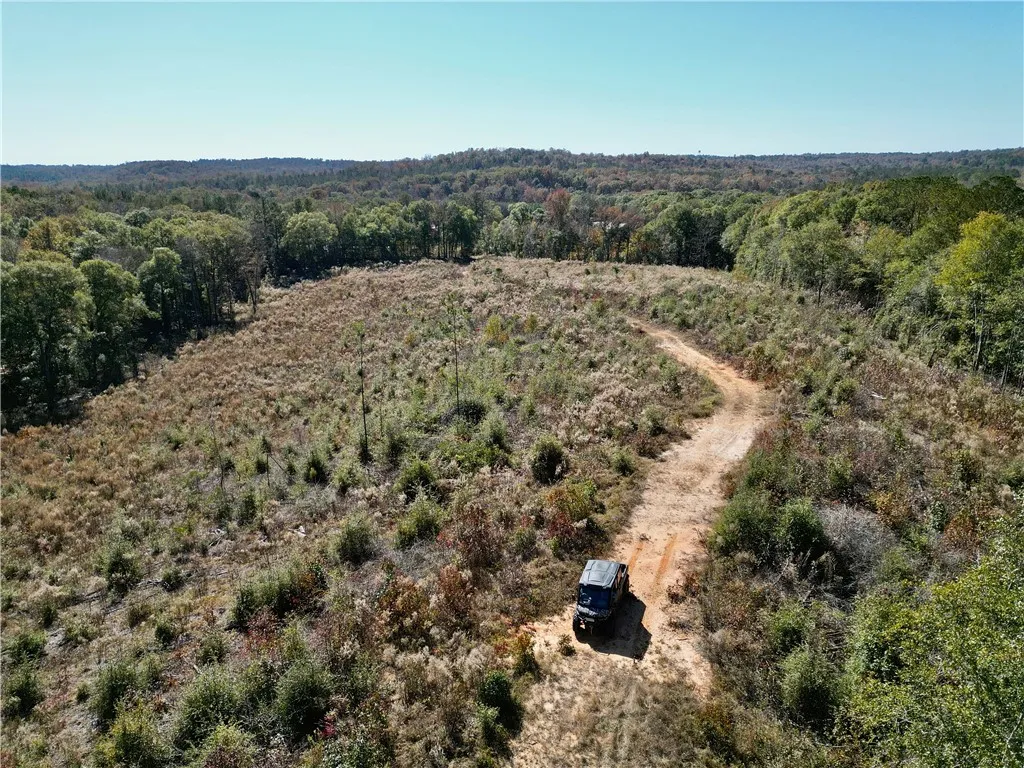 Vast acreage unfolds with a winding dirt path, leading through diverse natural landscapes.