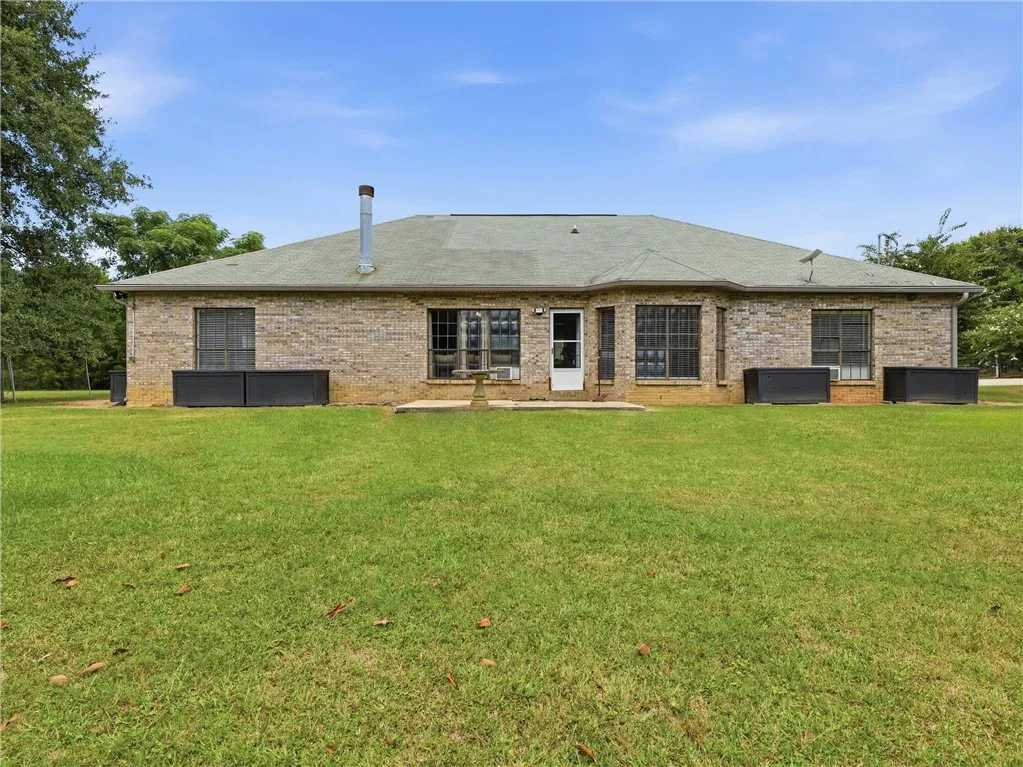 A spacious backyard leads to a classic brick residence with a paved patio.