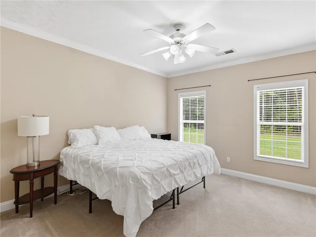 A well-lit bedroom with neutral walls offers two windows and a prominent ceiling fan.
