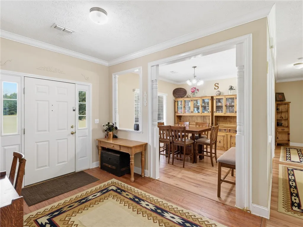 A well-lit entry hall with wood flooring opens to an adjoining dining area featuring a classic chandelier.