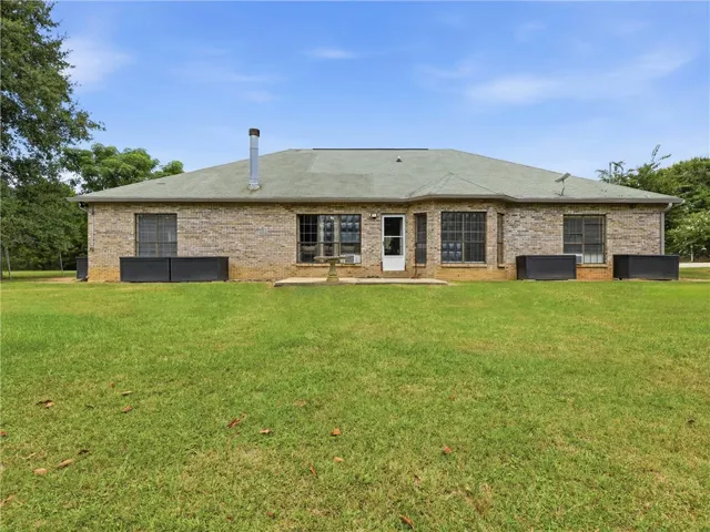 A spacious backyard leads to a classic brick residence with a paved patio.
