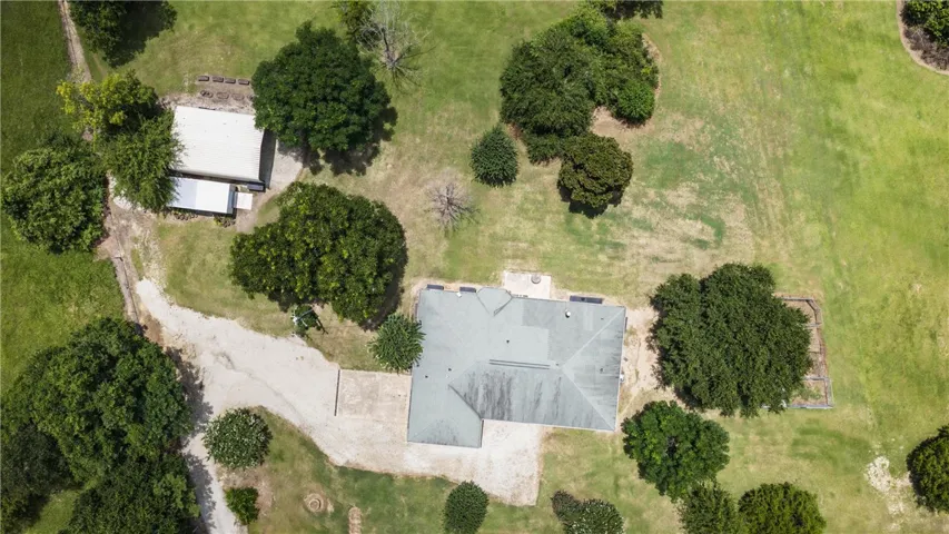 An aerial perspective reveals a vast, verdant lot encompassing a main residence and a detached structure, all connected by an extended driveway.
