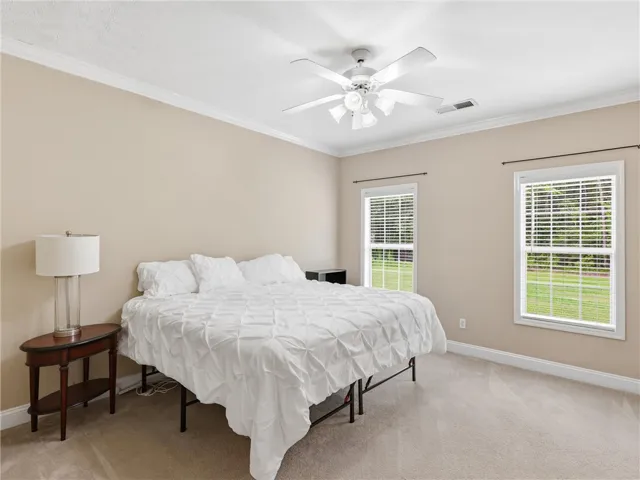 A well-lit bedroom with neutral walls offers two windows and a prominent ceiling fan.