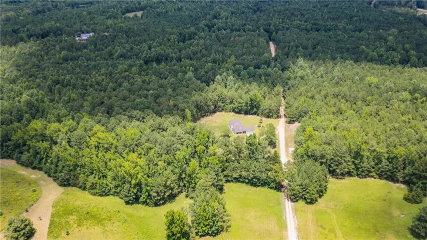 An aerial panorama reveals a secluded home nestled within verdant woodlands, accessible by a winding private drive.