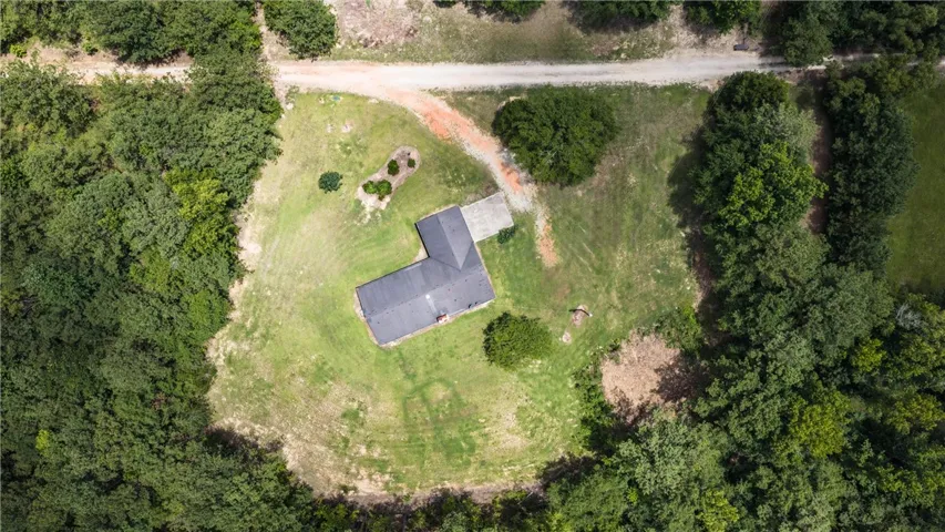 An aerial perspective reveals a secluded home amidst verdant trees and open land.