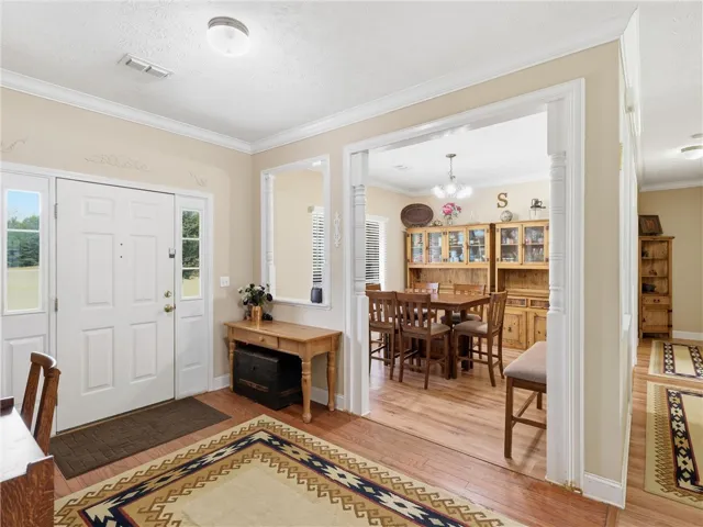 A well-lit entry hall with wood flooring opens to an adjoining dining area featuring a classic chandelier.