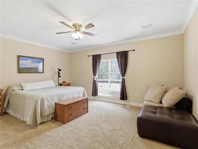 A tranquil sleeping area features a ceiling fan, crown molding, and plush carpeting.