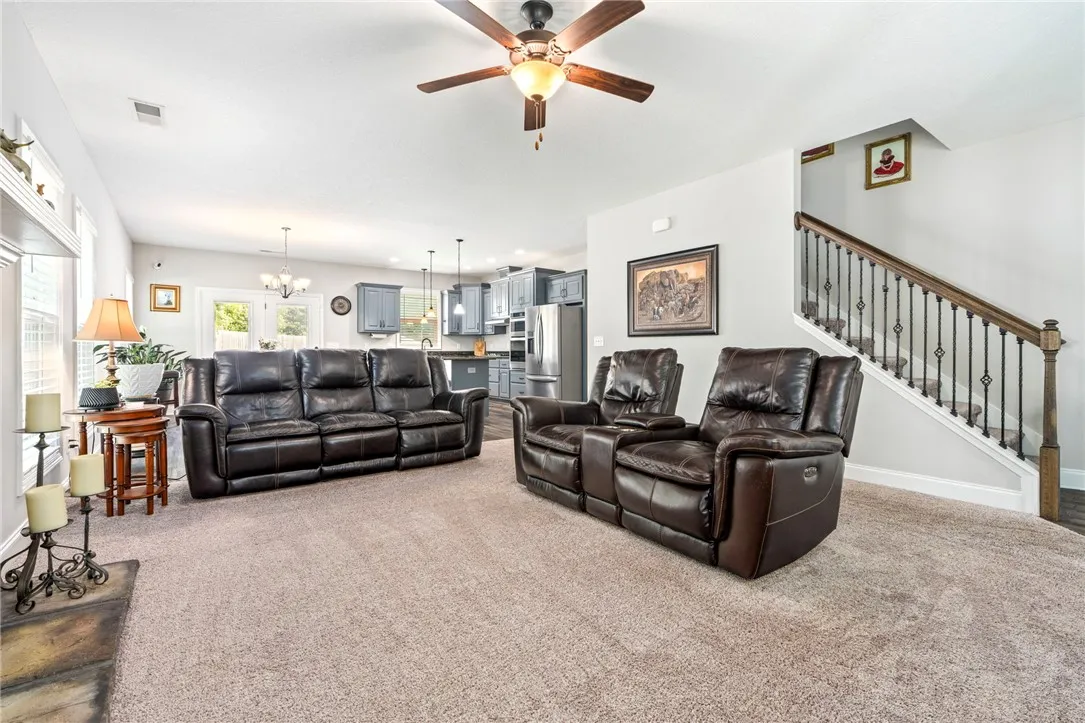 An open concept living area boasts a ceiling fan, plush carpeting, and seamless kitchen access.