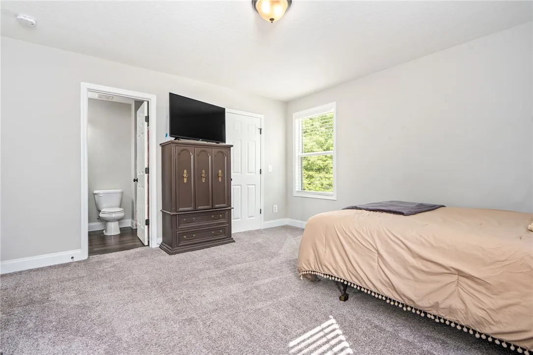 Comfortable carpeted primary bedroom featuring an en-suite bathroom access and a well-lit window overlooking natural views.