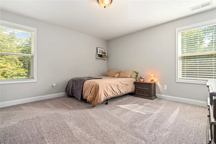 A well-lit room with ample space, featuring windows that offer views of surrounding greenery.