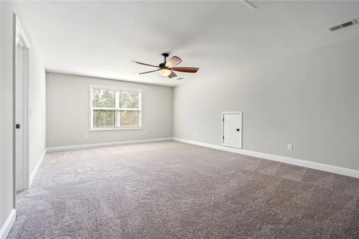 A well-lit, neutral-toned room features soft carpeting and a window overlooking lush greenery.