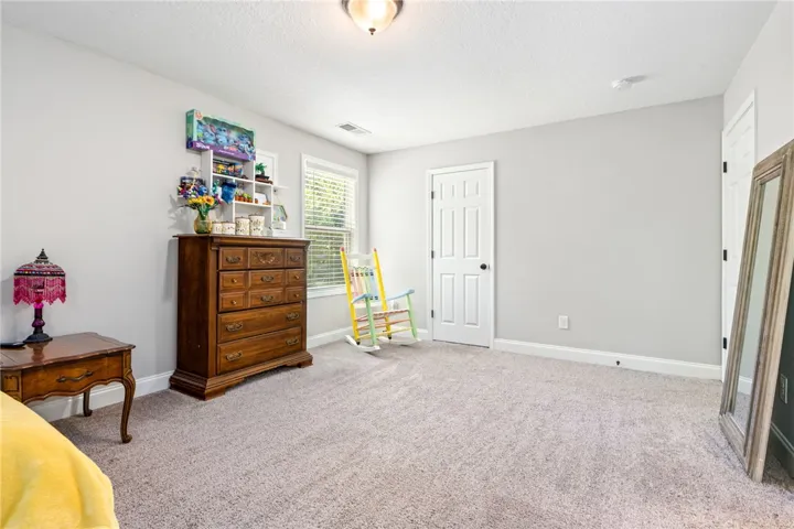 A well-lit bedroom features plush carpeting and abundant natural light from wide windows.
