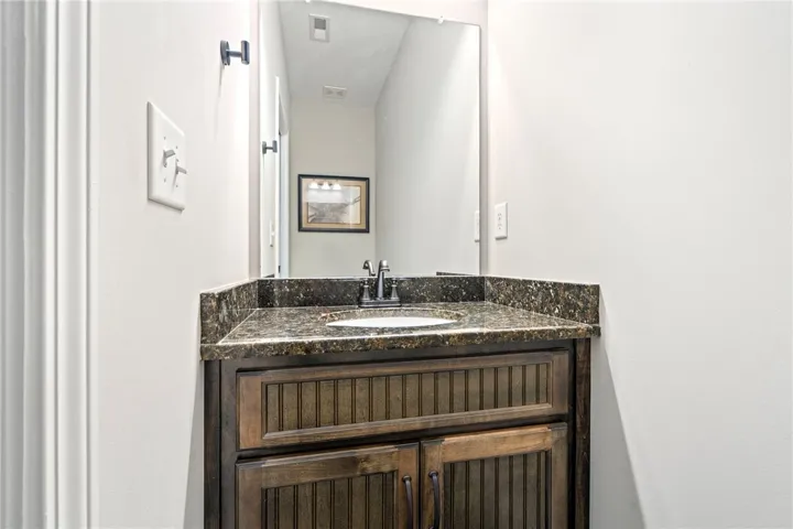 A dark wood vanity with a stone countertop and a simple mirror creates a functional powder room.