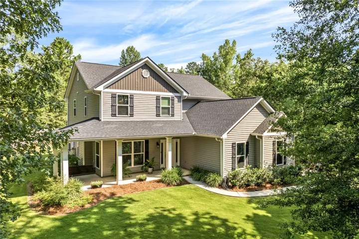 A classic facade with a welcoming covered porch, nestled amongst lush greenery and a manicured lawn.