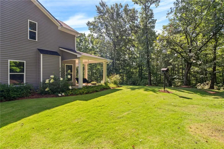 A well-maintained lawn and shaded porch offer a tranquil retreat surrounded by mature trees.