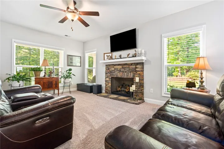 A comforting living area features a stone fireplace with a bright mantel, plush carpeting, and sun-drenched windows.