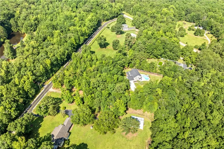 An aerial perspective reveals a secluded estate nestled among abundant mature trees, offering a private pool and vast green spaces.