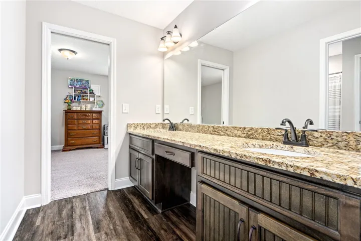 Double vanity with granite counters and rich cabinetry elevate this well-appointed primary bathroom.