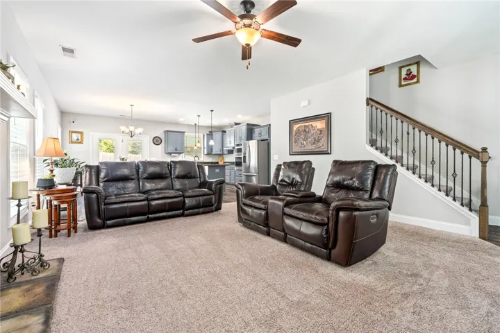 An open concept living area boasts a ceiling fan, plush carpeting, and seamless kitchen access.