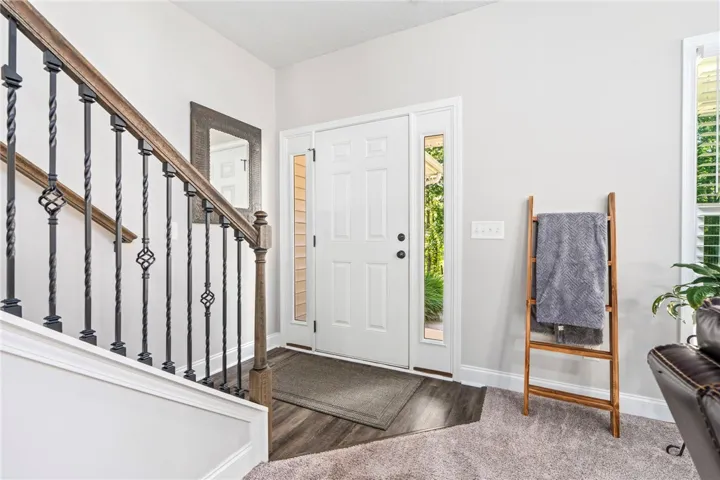 A graceful staircase with intricate iron balusters ascends from the warm wood flooring of the entry.