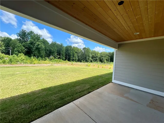 A tranquil outdoor living space features a covered patio opening to a sweeping green yard and verdant tree line.