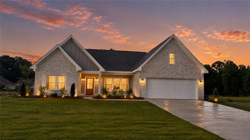 Illuminated brick and siding facade with gabled roofs welcomes you home under a vibrant twilight sky.