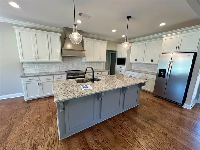 A well-lit kitchen featuring a spacious island, rich hardwood flooring, and stainless steel appliances.