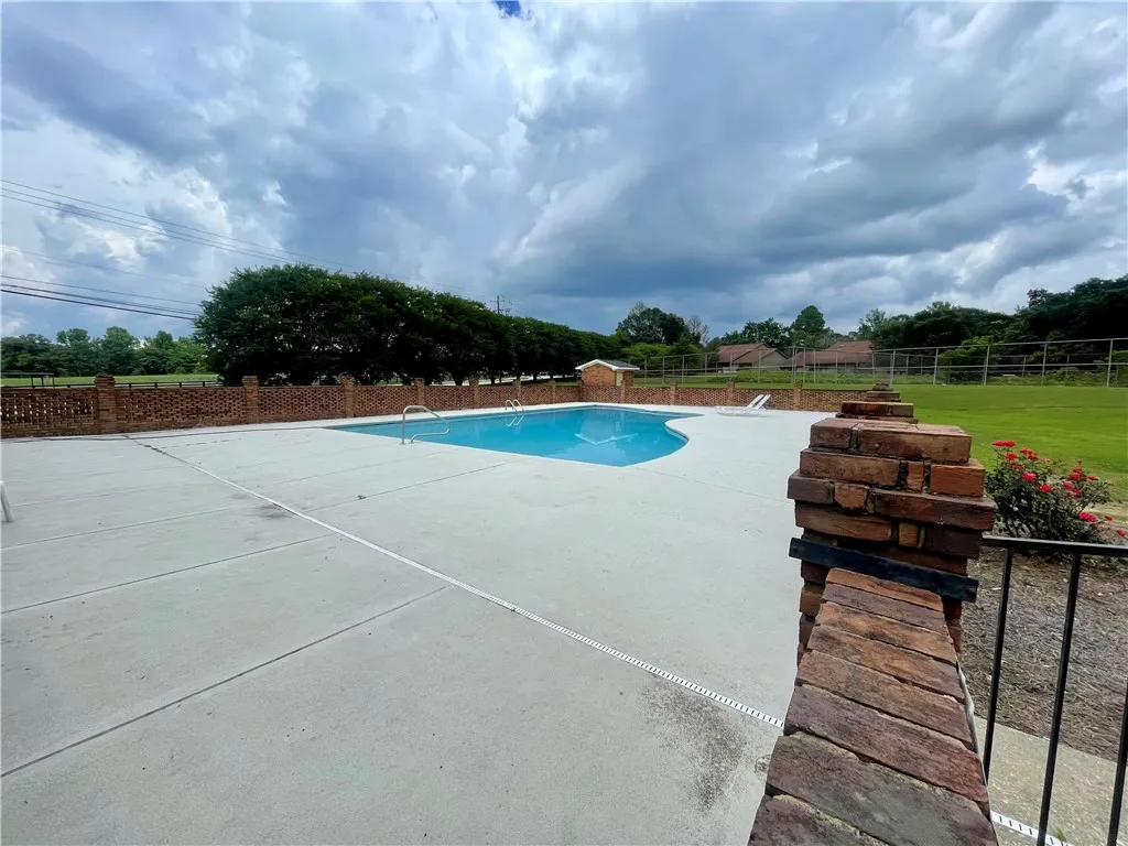 A refreshing swimming pool awaits, surrounded by a brick fence and ample patio space.