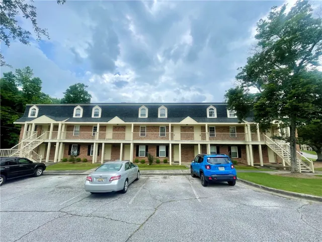 Multi-level residential building with ample parking, mature trees, and classic dormer windows.