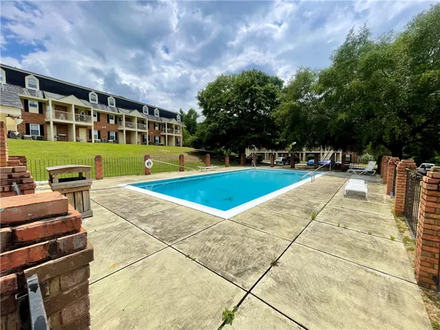 An inviting in-ground pool offers a refreshing escape, surrounded by concrete decking and lush green spaces.