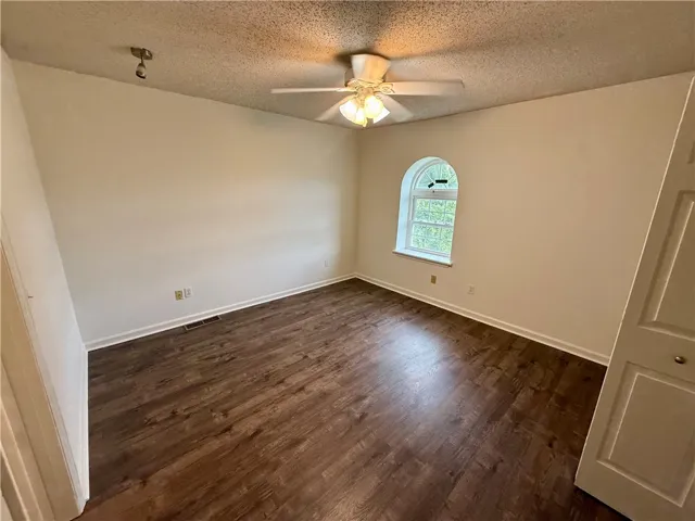 A well-lit bedroom features rich wood flooring and a unique arched window.