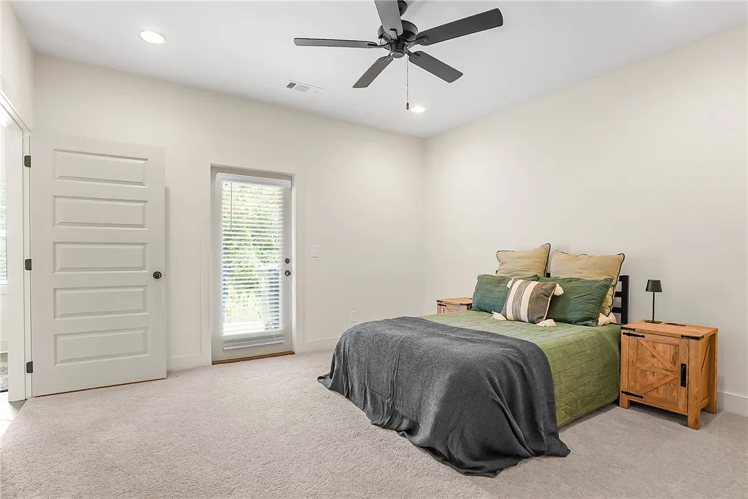 A tranquil bedroom features plush carpeting, a modern ceiling fan, and direct outdoor access through a glass-paneled door.