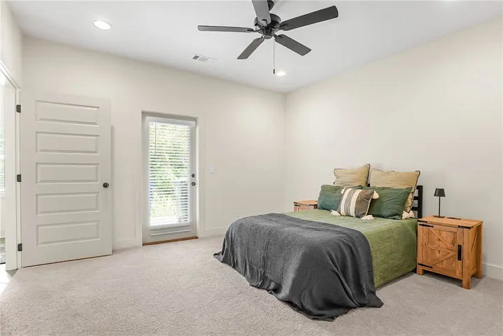 A tranquil bedroom features plush carpeting, a modern ceiling fan, and direct outdoor access through a glass-paneled door.