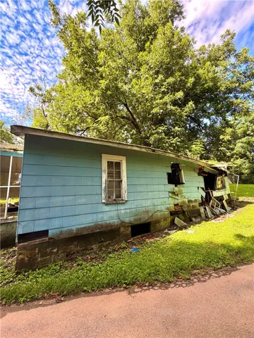 A forgotten dwelling awaits transformation, hinting at a past life beneath mature shade trees.