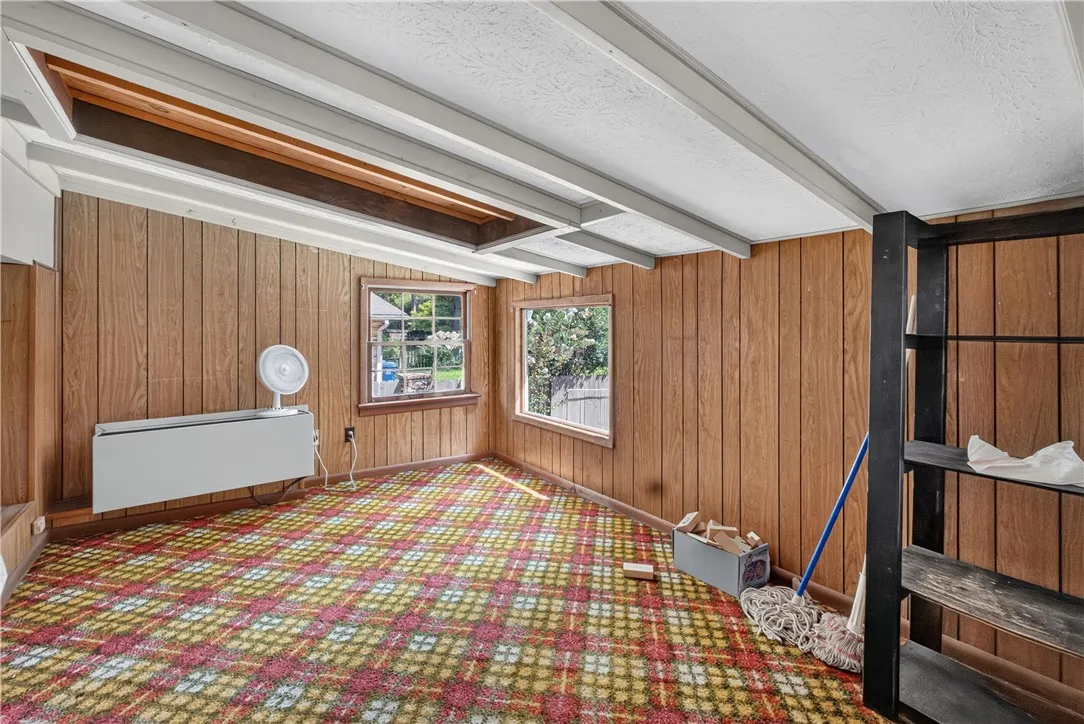 A quaint room with wood paneling and plaid carpet offers a cozy, unique space with natural light.
