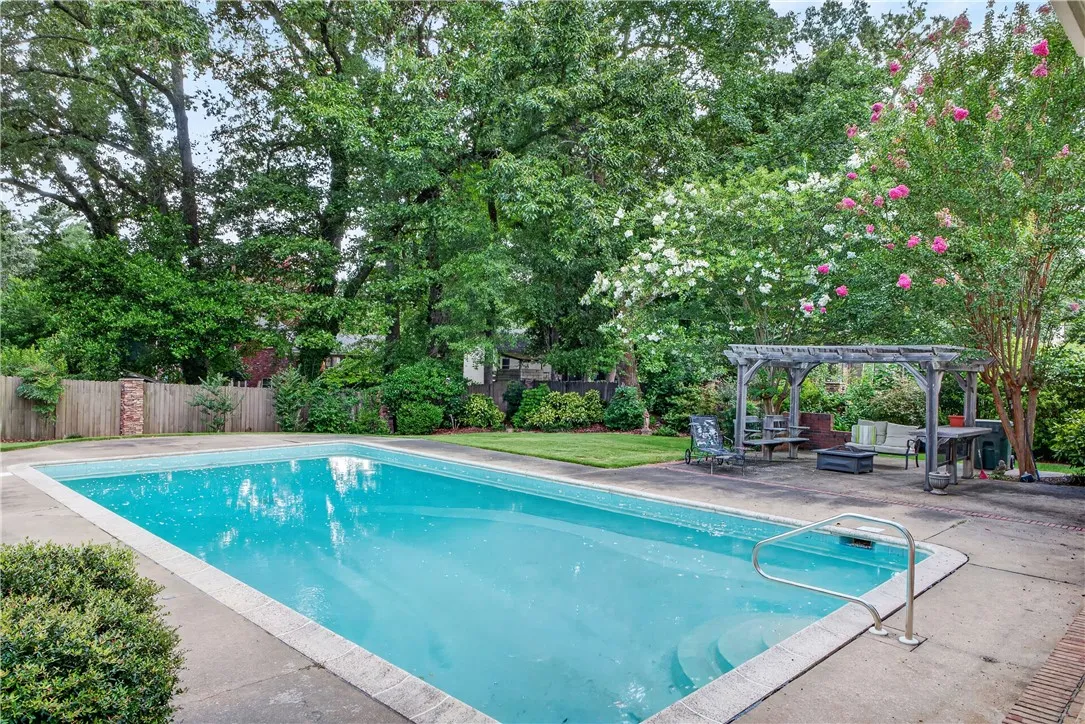 An inviting backyard oasis offers a sparkling in-ground pool complemented by a charming pergola-covered patio area for outdoor relaxation.