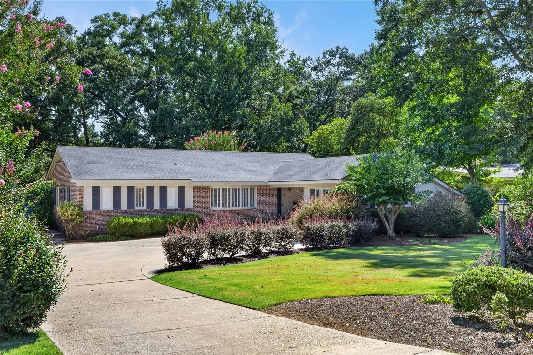 Mature trees frame this brick-accented residence, featuring a curved driveway and well-tended landscaping.