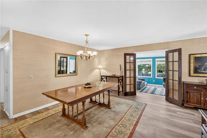French doors open into a bright, airy dining space featuring a polished wooden table and decorative chandelier.