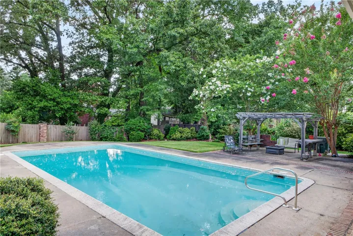 An inviting backyard oasis offers a sparkling in-ground pool complemented by a charming pergola-covered patio area for outdoor relaxation.