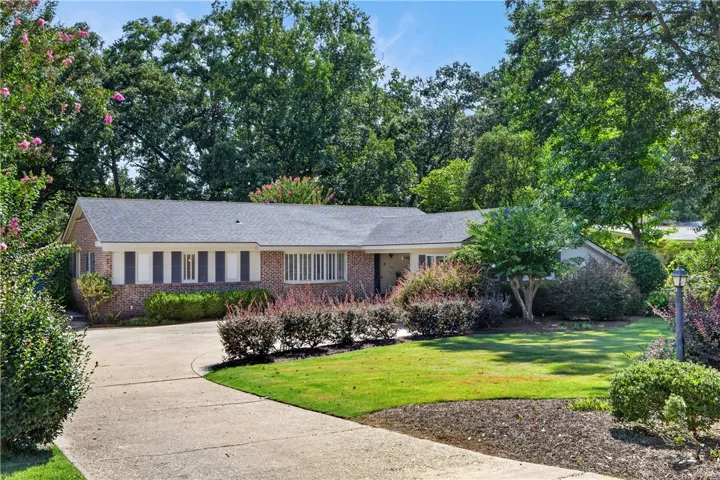 Mature trees frame this brick-accented residence, featuring a curved driveway and well-tended landscaping.