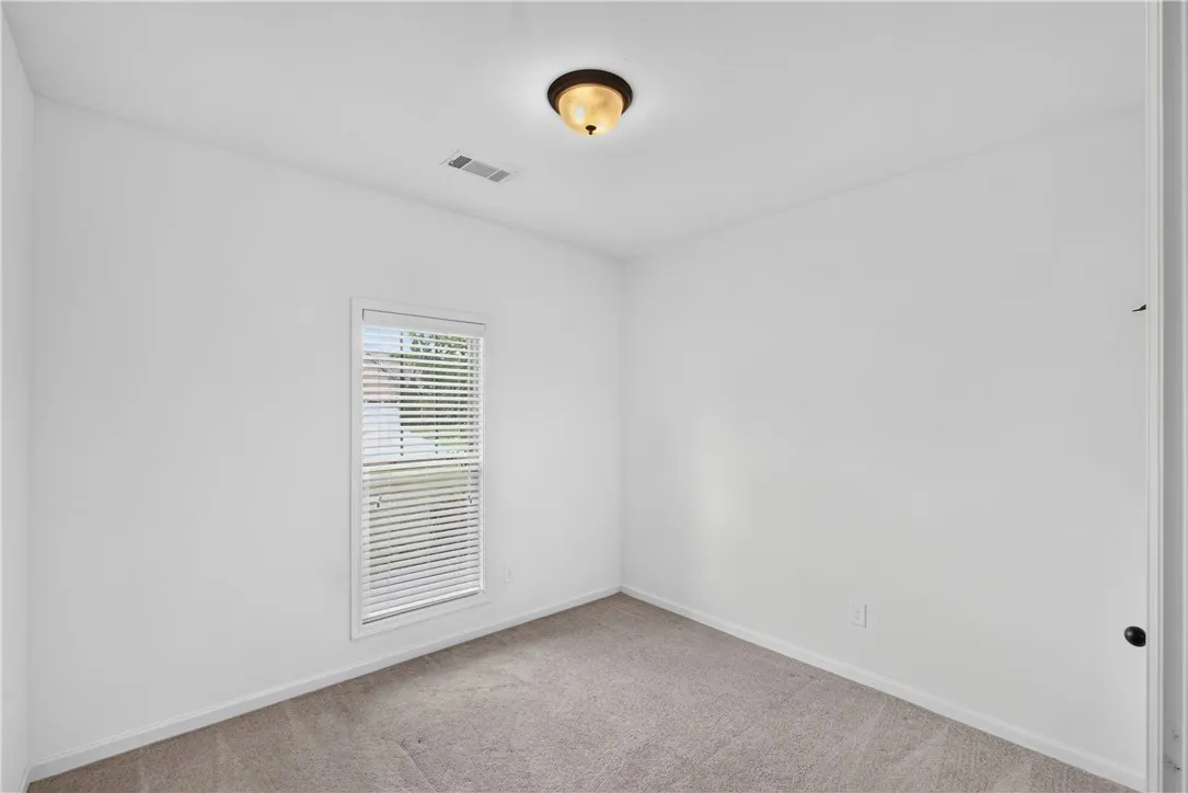 A well-lit bedroom features plush carpeting and a bright window, creating a comfortable and inviting atmosphere.