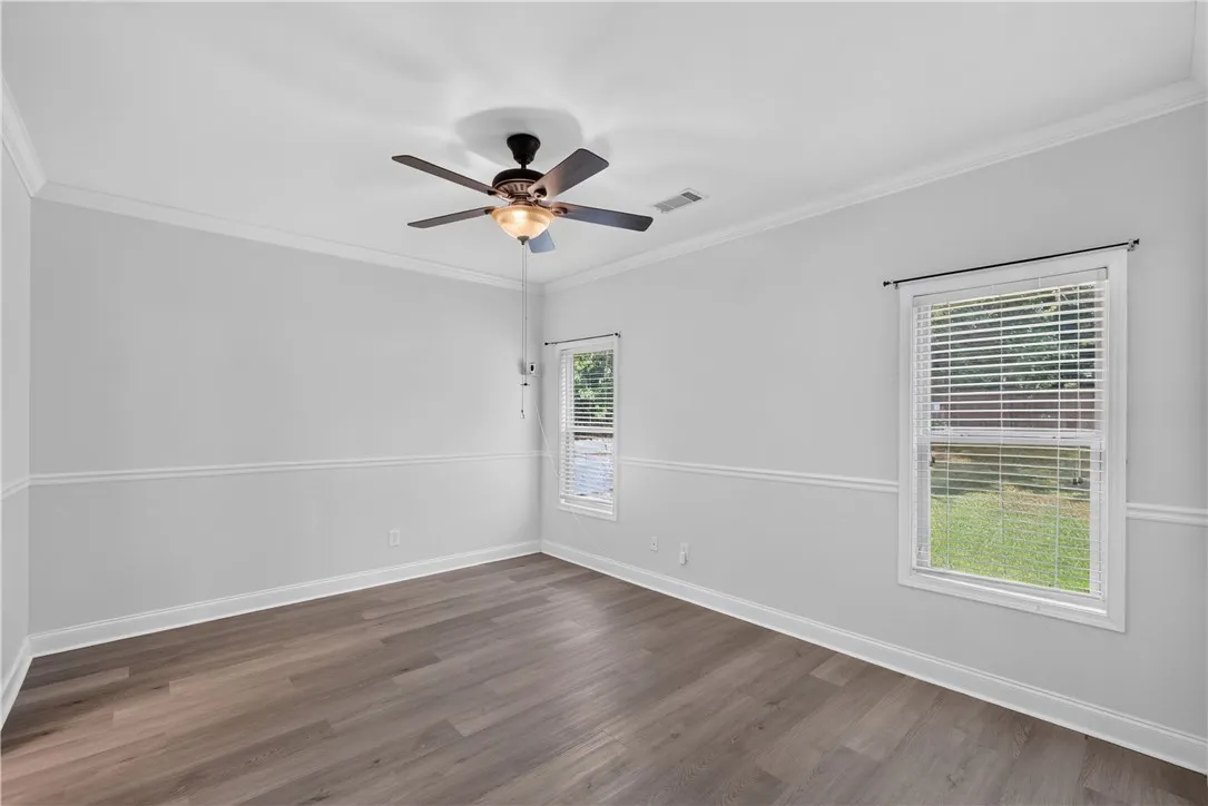 Well-lit room featuring crown molding, durable flooring, and two large windows offering verdant views.