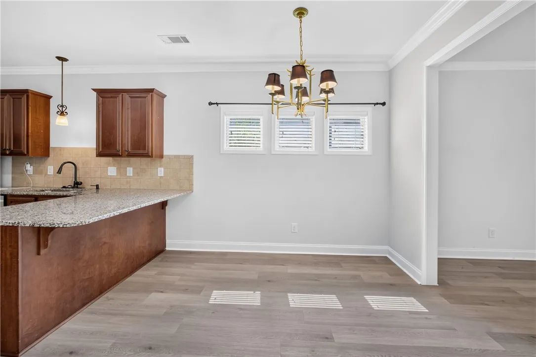A luminous dining space features a sophisticated chandelier, sleek wood flooring, and an adjoining kitchen with granite counters.