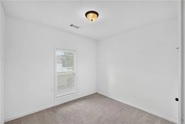 A well-lit bedroom features plush carpeting and a bright window, creating a comfortable and inviting atmosphere.